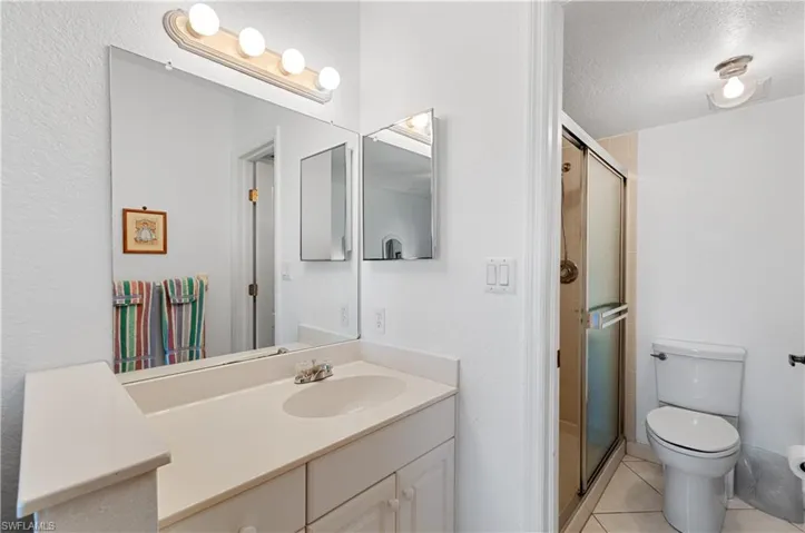 Bathroom with a shower with shower door, a textured ceiling, tile patterned flooring, vanity, and toilet