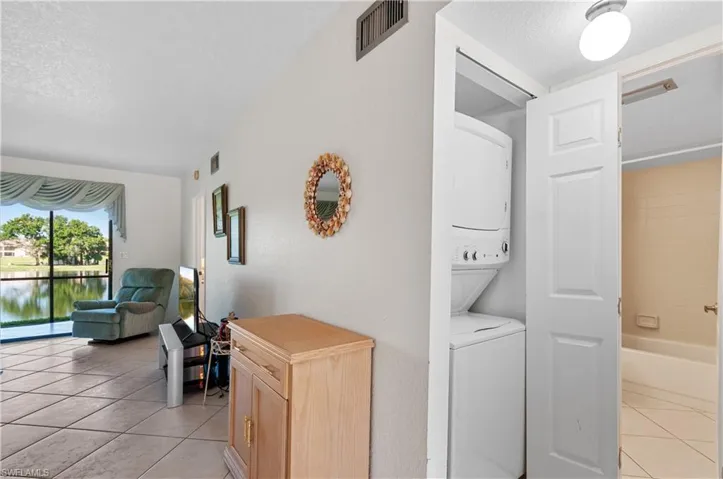 Hall with light tile patterned floors, stacked washing maching and dryer, and a textured ceiling