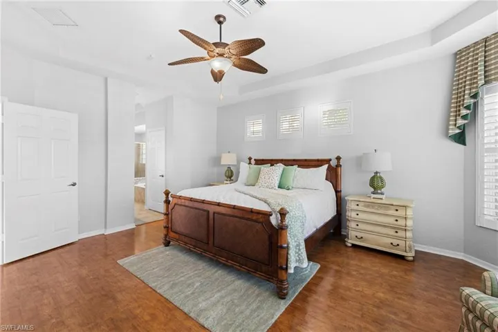 Bedroom with dark wood-style flooring, ceiling fan, ensuite bathroom, and a tray ceiling