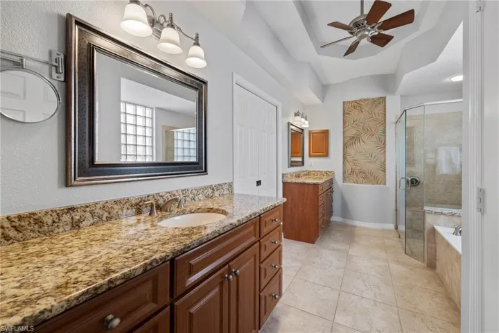 Bathroom featuring two vanities, a stall shower, a ceiling fan, light tile patterned floors, and a bath