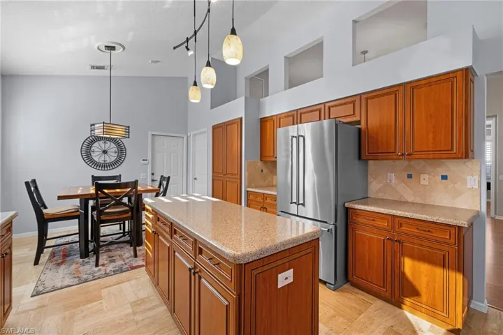 Kitchen with decorative light fixtures, brown cabinetry, freestanding refrigerator, decorative backsplash, and a high ceiling