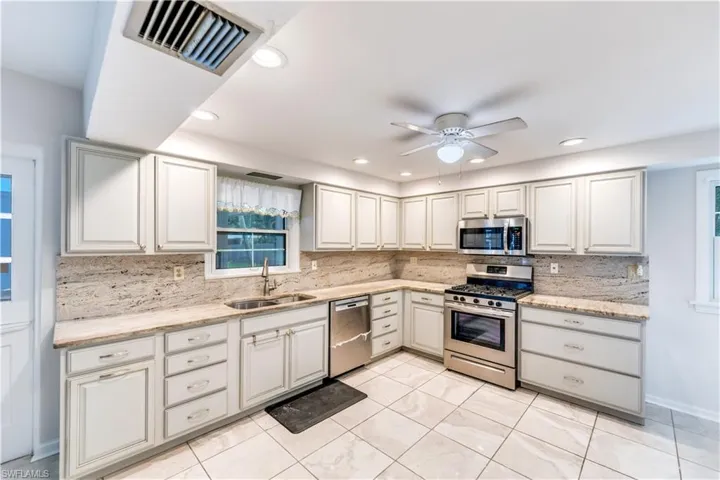 Kitchen with ceiling fan, tasteful backsplash, light tile floors, sink, and appliances with stainless steel finishes