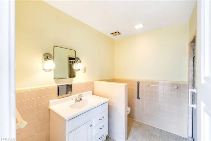 Bathroom featuring tile flooring, tile walls, backsplash, vanity, and toilet