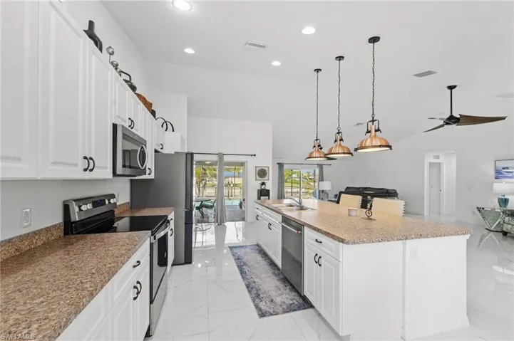 Kitchen with stainless steel appliances, a spacious island, white cabinetry, open floor plan, and light marble finish floors