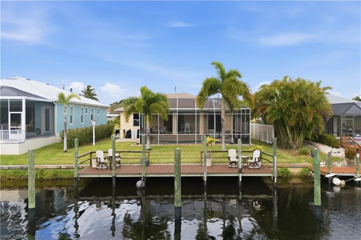 Waterfront property featuring a private boat dock, lush green lawn, and mature palm trees