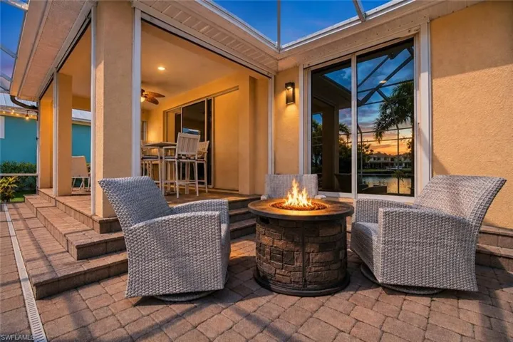 Expansive paver patio featuring a stone-clad fire pit, sliding glass doors, and a covered lanai with integrated lighting