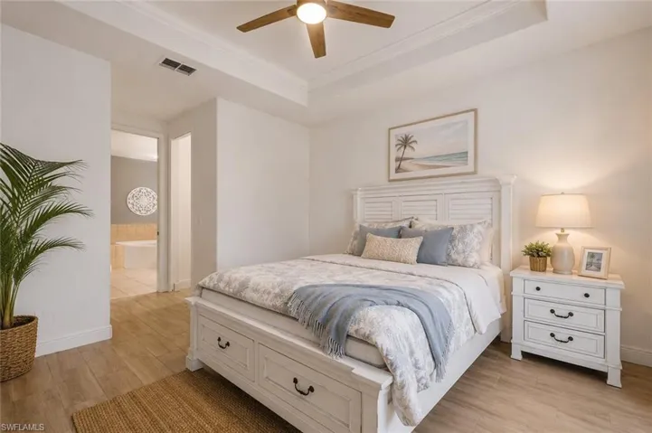 Spacious bedroom featuring wood-finish flooring, a tray ceiling with a ceiling fan, and white baseboards