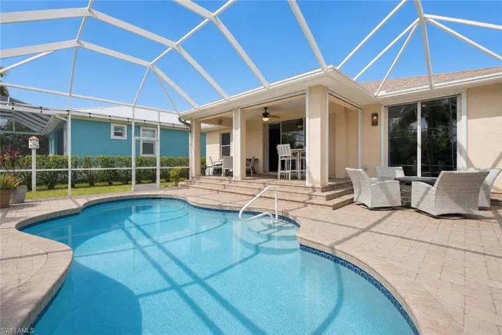 Screened outdoor living area featuring a freeform swimming pool with a tiled edge, a paver patio, a covered lanai with a ceiling fan, and sliding glass doors