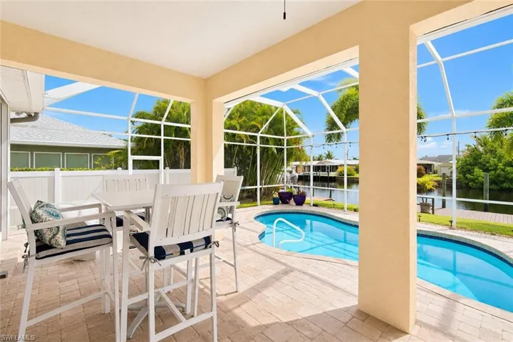 Screened lanai featuring a paver patio, a freeform swimming pool, a canal, mature tropical landscaping, and a privacy fence