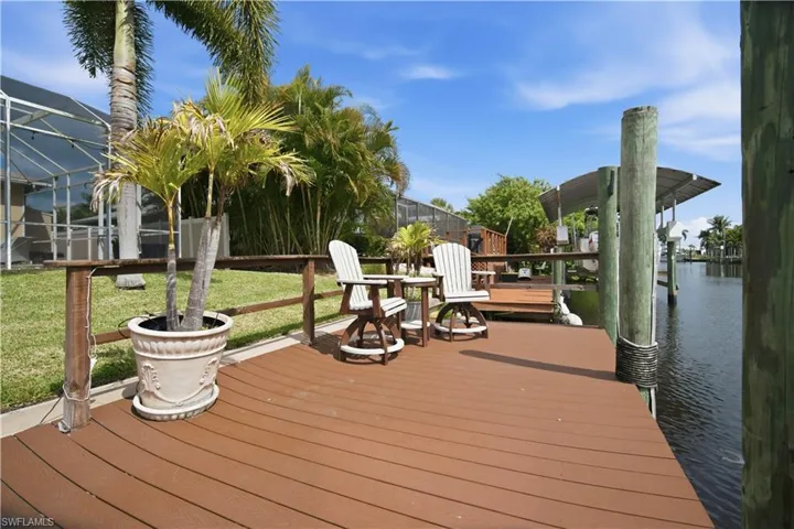 Waterfront composite deck featuring a wooden railing, pilings, and a boat canopy