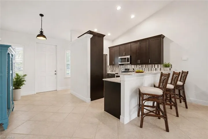 Kitchen featuring dark wood-finish cabinetry, stainless steel appliances, a multi-tone tile backsplash, and a breakfast bar with a light-colored countertop