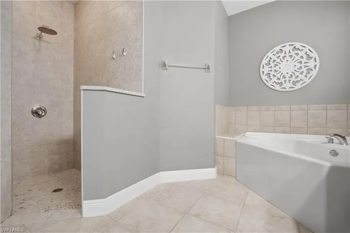 Walk-in shower with rain showerhead, pebble-style flooring, and stone-look wall tiles