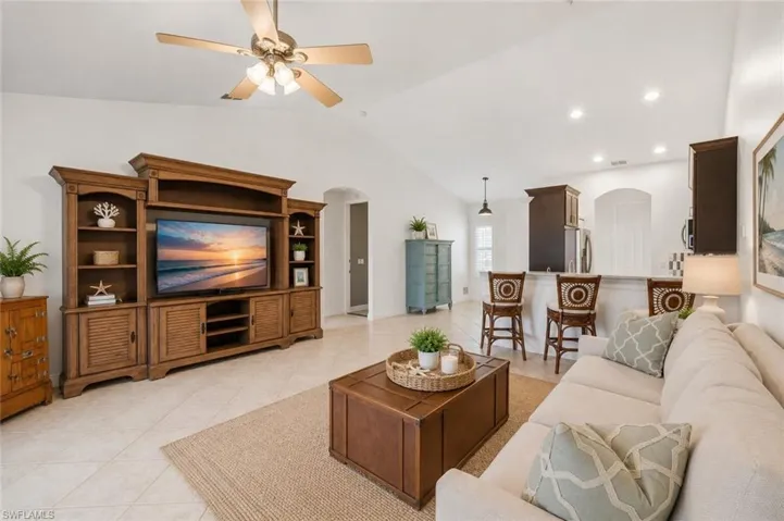 Spacious living area featuring vaulted ceilings, a built-in entertainment center, tile flooring, and a ceiling fan with integrated lighting