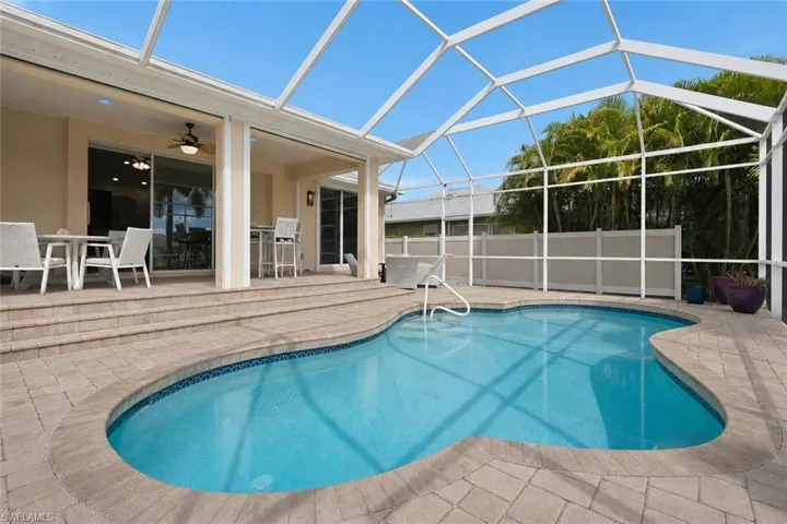 Screened-in pool deck featuring a freeform swimming pool, paver hardscaping, a multi-tiered patio, and a covered lanai with exterior lighting