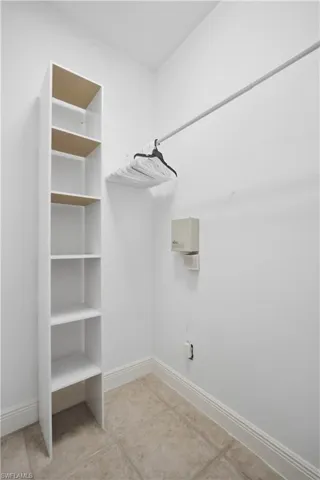Primary closet featuring built-in shelving, a garment rod, tile flooring, and white baseboards