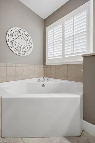 Corner soaking tub with polished chrome fixtures, surrounded by neutral-toned tile