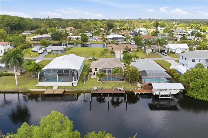 Waterfront property featuring a screened-in pool enclosure, mature palm trees, and a private dock with direct canal access