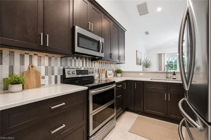 Kitchen featuring dark wood cabinetry, light-toned countertops, stainless steel appliances, and a mosaic tile backsplash