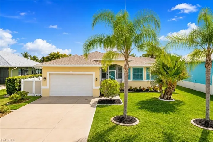 Single-story residence featuring a two-car garage, concrete driveway, and a well-maintained front lawn with mature palm trees