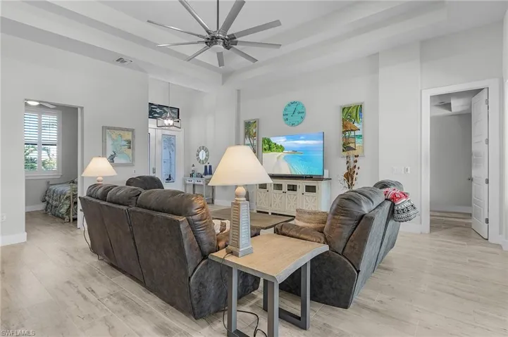 Living room featuring light tile floors, a tray ceiling, and ceiling fan