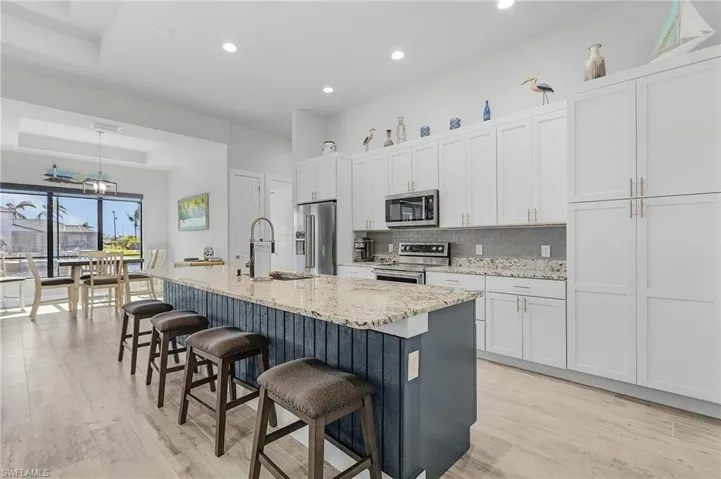 Kitchen with appliances with stainless steel finishes, sink, an island with sink, white cabinets, and light tile flooring