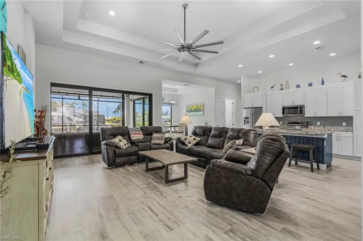 Living room featuring ceiling fan with notable chandelier, light tile flooring, and a raised ceiling