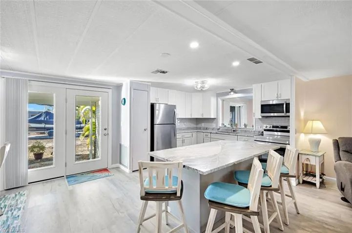 Bright, open-concept kitchen featuring white cabinetry, quartz countertops, stainless steel appliances, and a spacious island with seating.