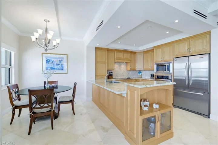 Kitchen featuring light brown cabinetry, appliances with stainless steel finishes, a chandelier, ornamental molding, and backsplash