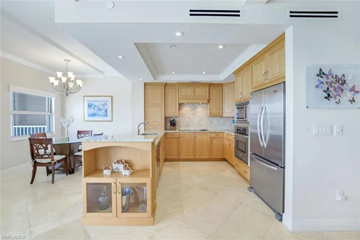 Kitchen with light brown cabinetry, a chandelier, tasteful backsplash, appliances with stainless steel finishes, and ornamental molding