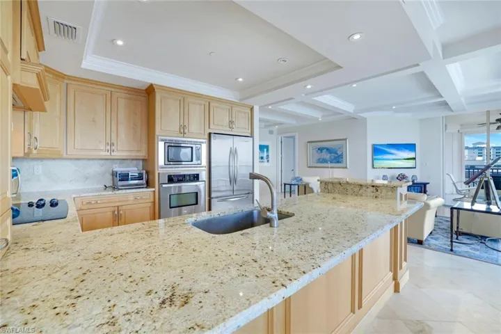 Kitchen featuring light brown cabinetry, light stone counters, coffered ceiling, stainless steel appliances, and tasteful backsplash