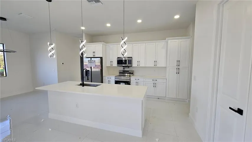 Kitchen featuring pendant lighting, white cabinetry, appliances with stainless steel finishes, and a kitchen island with sink