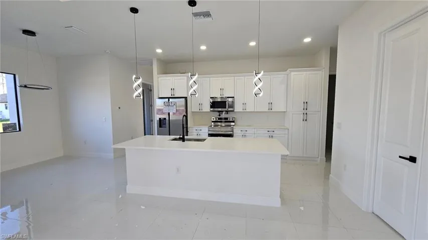 Kitchen featuring appliances with stainless steel finishes, pendant lighting, sink, white cabinets, and a kitchen island with sink