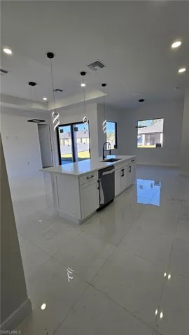 Kitchen with pendant lighting, dishwasher, sink, white cabinets, and a center island