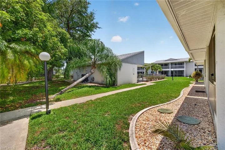 Exterior walkway with a decorative rock bed, mature palm trees, and lush green lawn
