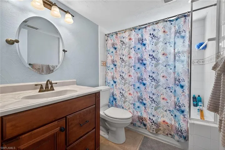 Bathroom featuring a single vanity with an oval mirror, a shower-tub combination with a glass panel, and light-toned wall paint