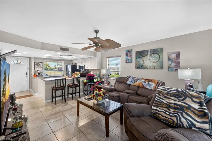 Open-concept living space featuring neutral tile flooring, a ceiling fan, and a kitchen pass-through with a breakfast bar