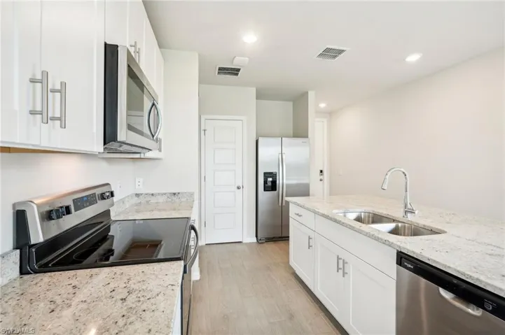 Kitchen with white cabinets, light stone countertops, stainless steel appliances, light hardwood / wood-style flooring, and sink