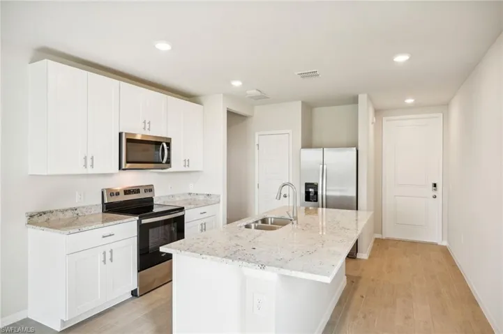 Kitchen with appliances with stainless steel finishes, sink, light hardwood / wood-style flooring, and an island with sink