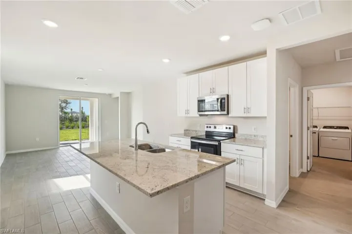 Kitchen with white cabinetry, an island with sink, stainless steel appliances, sink, and washer and dryer