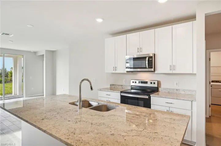 Kitchen with light hardwood / wood-style floors, white cabinets, light stone countertops, stainless steel appliances, and sink