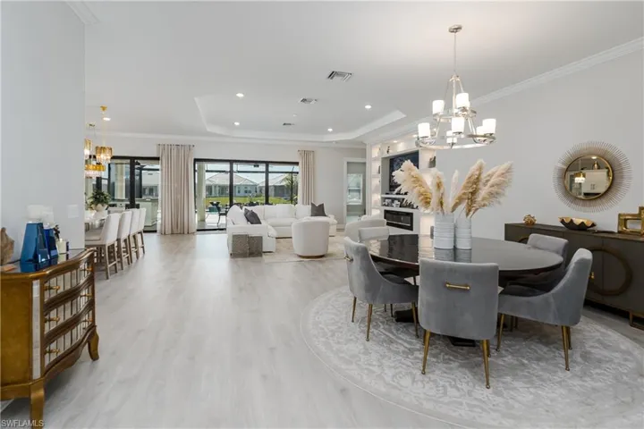 Dining area with a chandelier, a raised ceiling, wood finished floors, crown molding, and recessed lighting