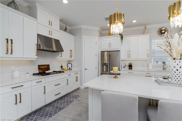 Kitchen featuring stainless steel fridge with ice dispenser, under cabinet range hood, a chandelier, gas cooktop, and white cabinets