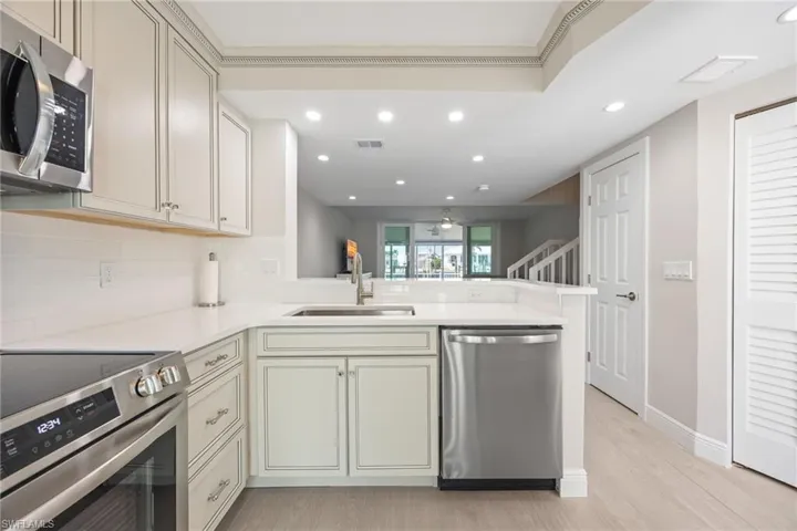 Open kitchen with light colored cabinets, tray ceiling and beautiful countertops