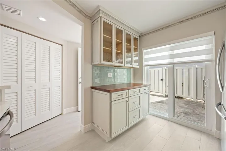 Kitchen with glass insert cabinets, backsplash, wooden counters, stainless steel appliances, and ornamental molding
