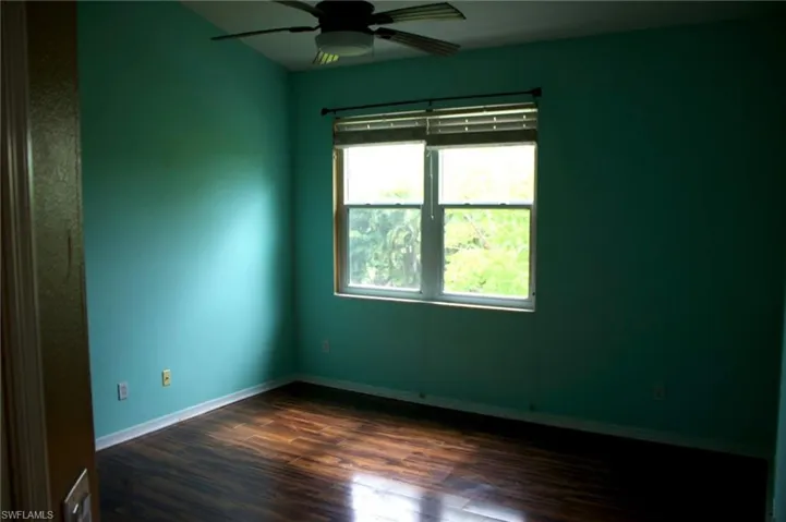 Spacious room featuring wood-finish flooring, a ceiling fan, and a large window with horizontal blinds