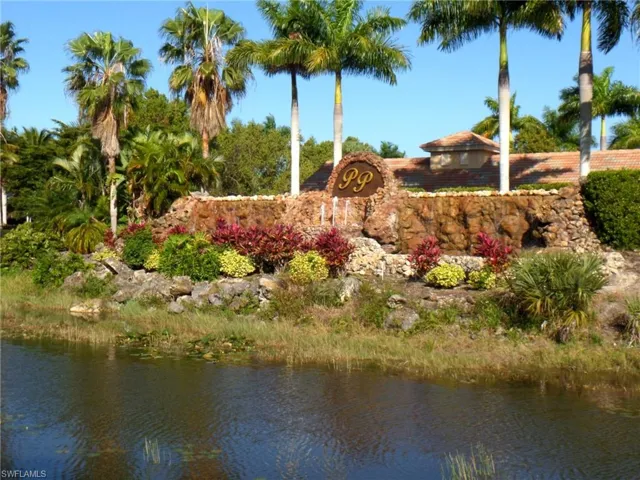 Prominent stone-faced entry monument with a water feature, lush tropical landscaping, and mature palm trees