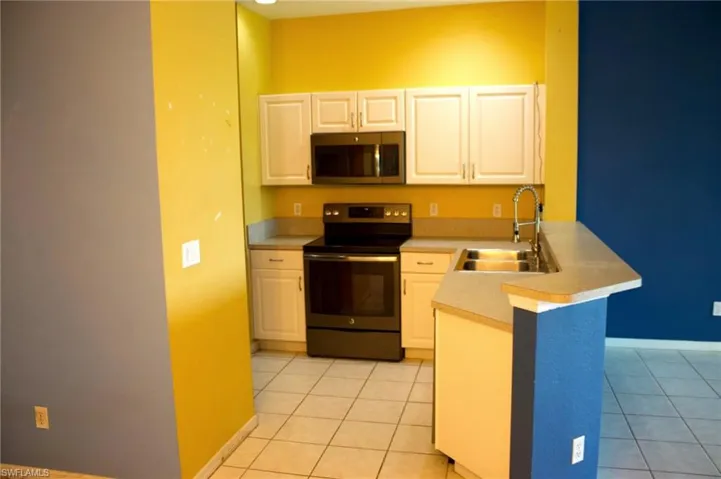 Kitchen featuring white cabinetry, black appliances, a double basin sink with a high-arc faucet, and tiled flooring