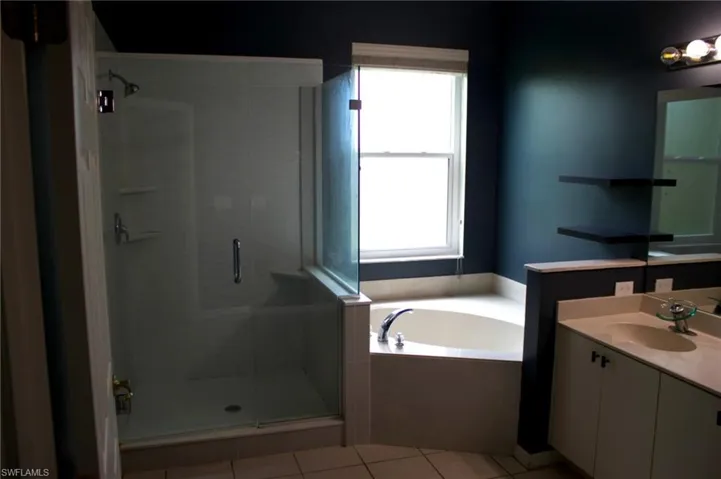 Bathroom featuring a glass-enclosed shower, a built-in corner soaking tub, a double vanity with an integrated countertop, and a window
