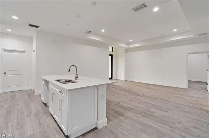 Kitchen featuring sink, light hardwood / wood-style flooring, white cabinetry, and a kitchen island with sink