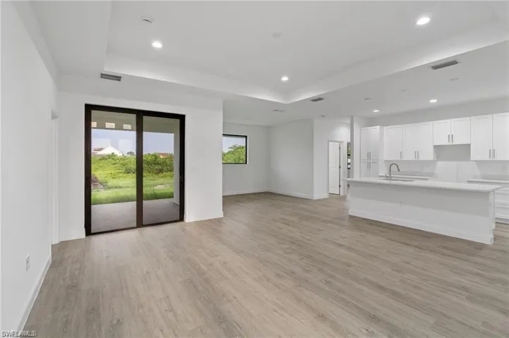 Unfurnished living room with sink, a tray ceiling, and light hardwood / wood-style floors